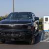 Chevrolet's electric pickup truck EV at a charger, trees and fields visible in the background.