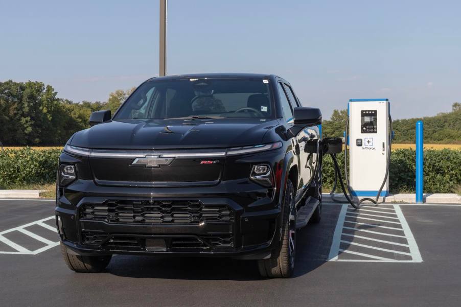 Chevrolet's electric pickup truck EV at a charger, trees and fields visible in the background.