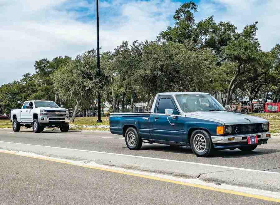 White chevrolet Silverado and classic Toyota pickup truck on the road.
