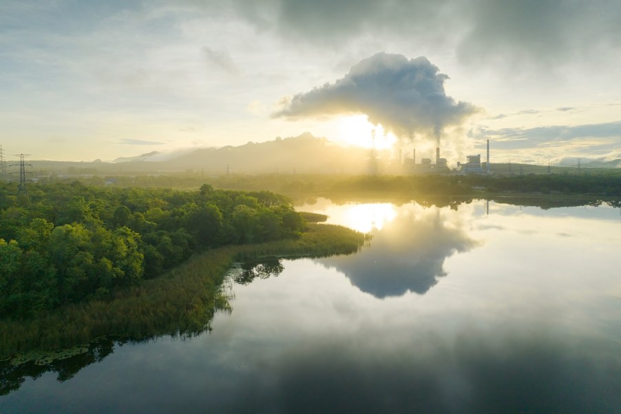Steam rising above a coal power plant, the sun rising over a lake in the foreground.