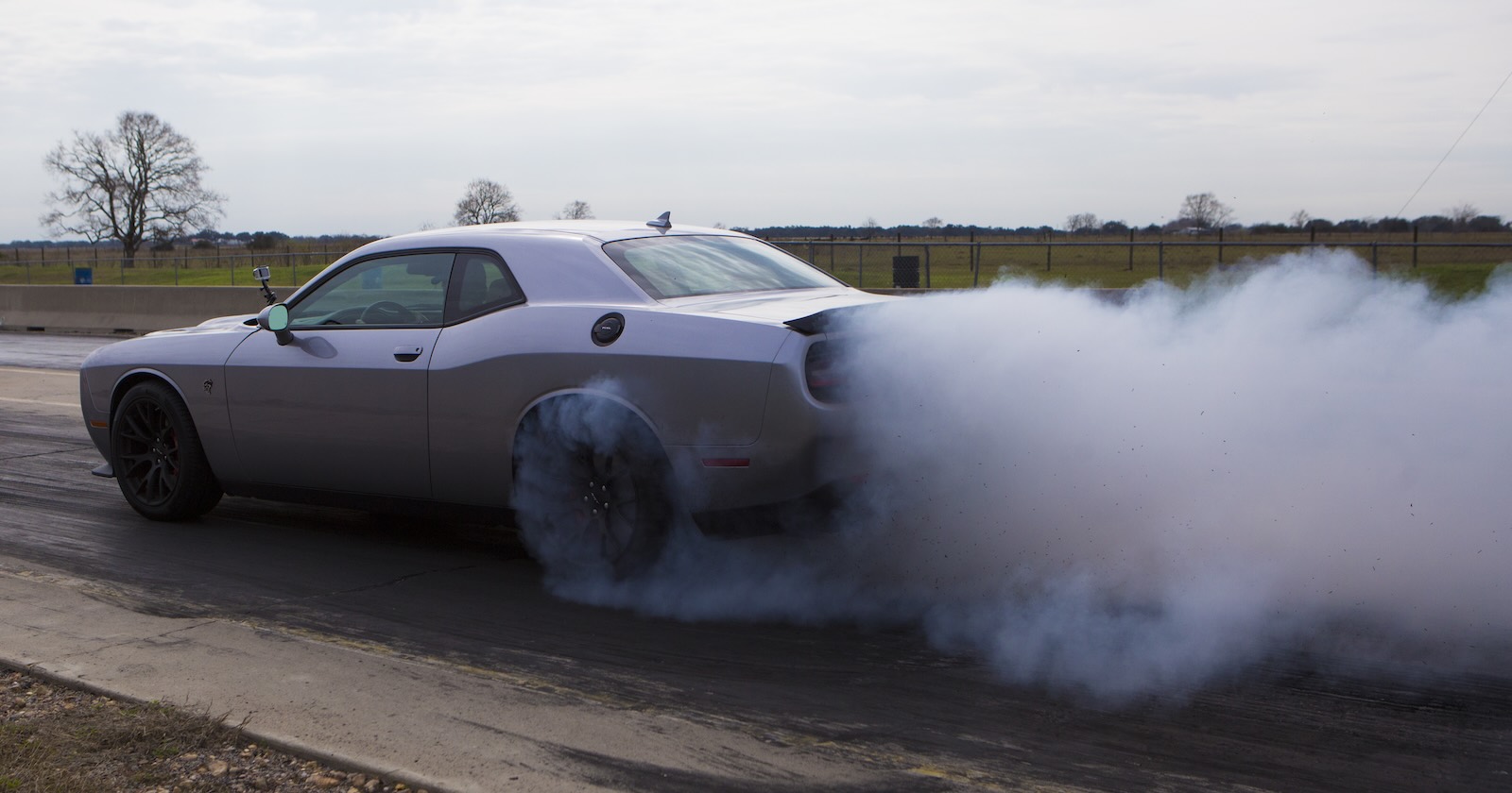 Silver Dodge Challenger Hellcat doing burnouts on a race track.