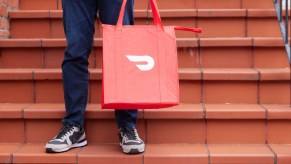 Driver holds a red DoorDash bag on the steps of a family's home.
