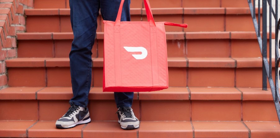 Driver holds a red DoorDash bag on the steps of a family's home.