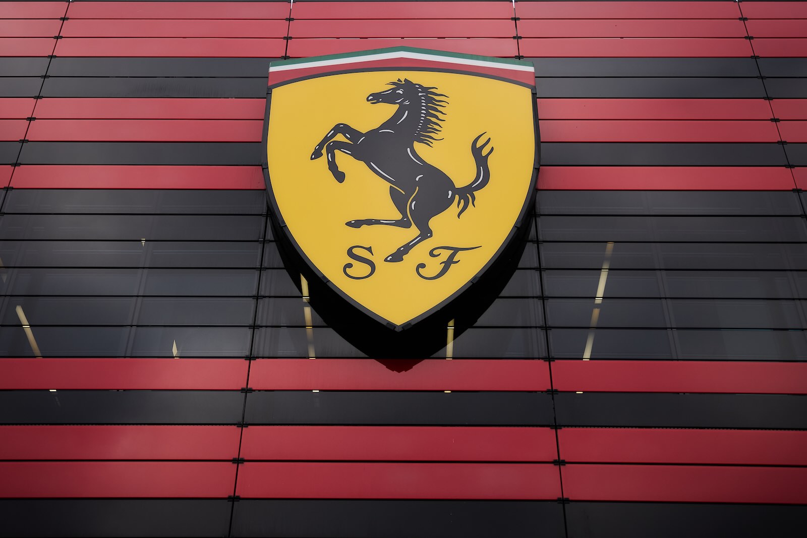 Ferrari's yellow shield prancing pony logo on a black and red striped background.