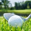 Golf ball and club on a course, pond visible in the background.