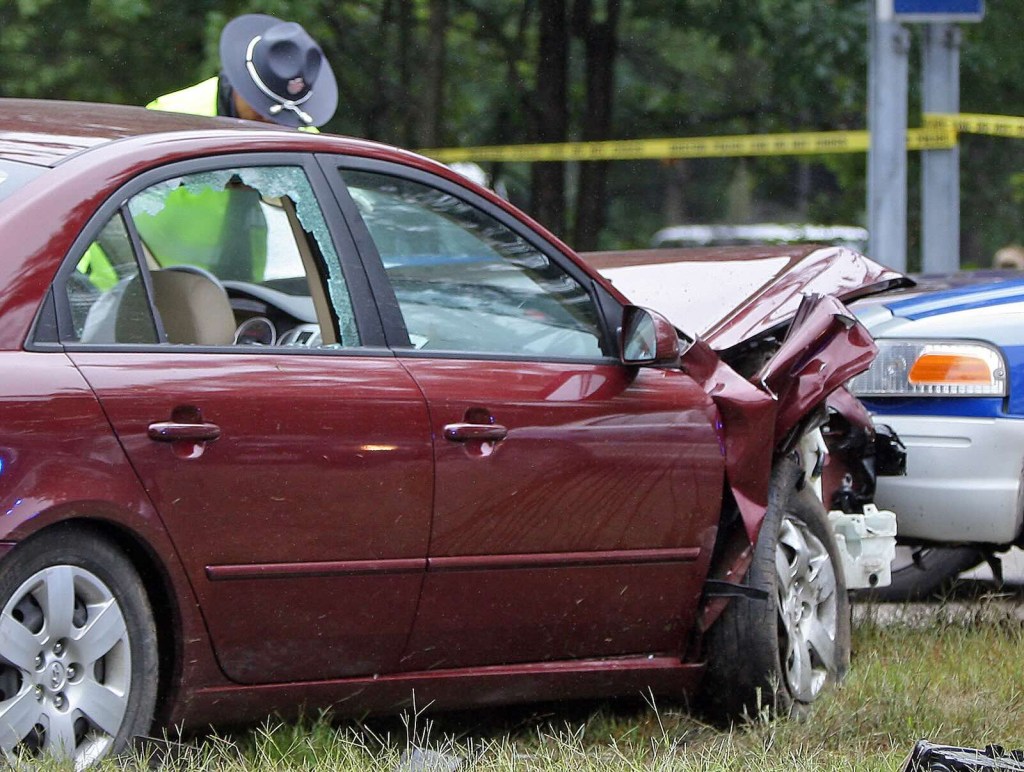 Red Hyundai Sonata sedan, smashed up during a police chase, with officers examining it.