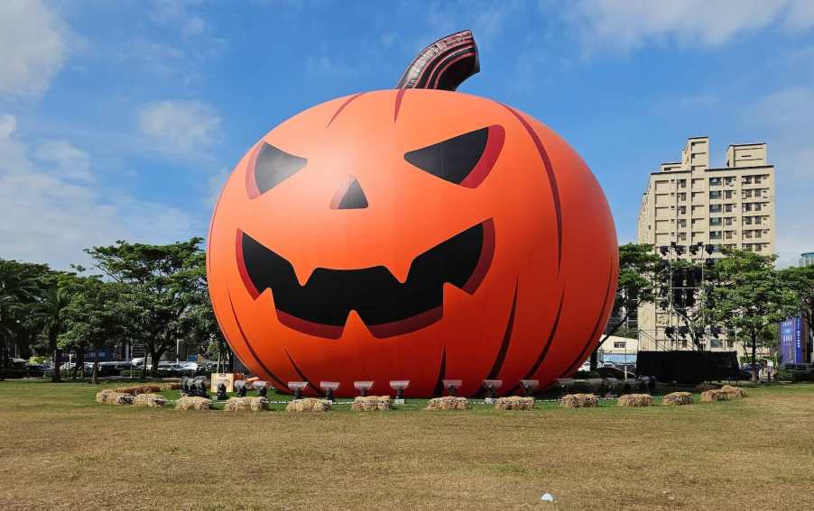 Inflatable orange pumpkin ornament on a lawn, buildings visible in the background.