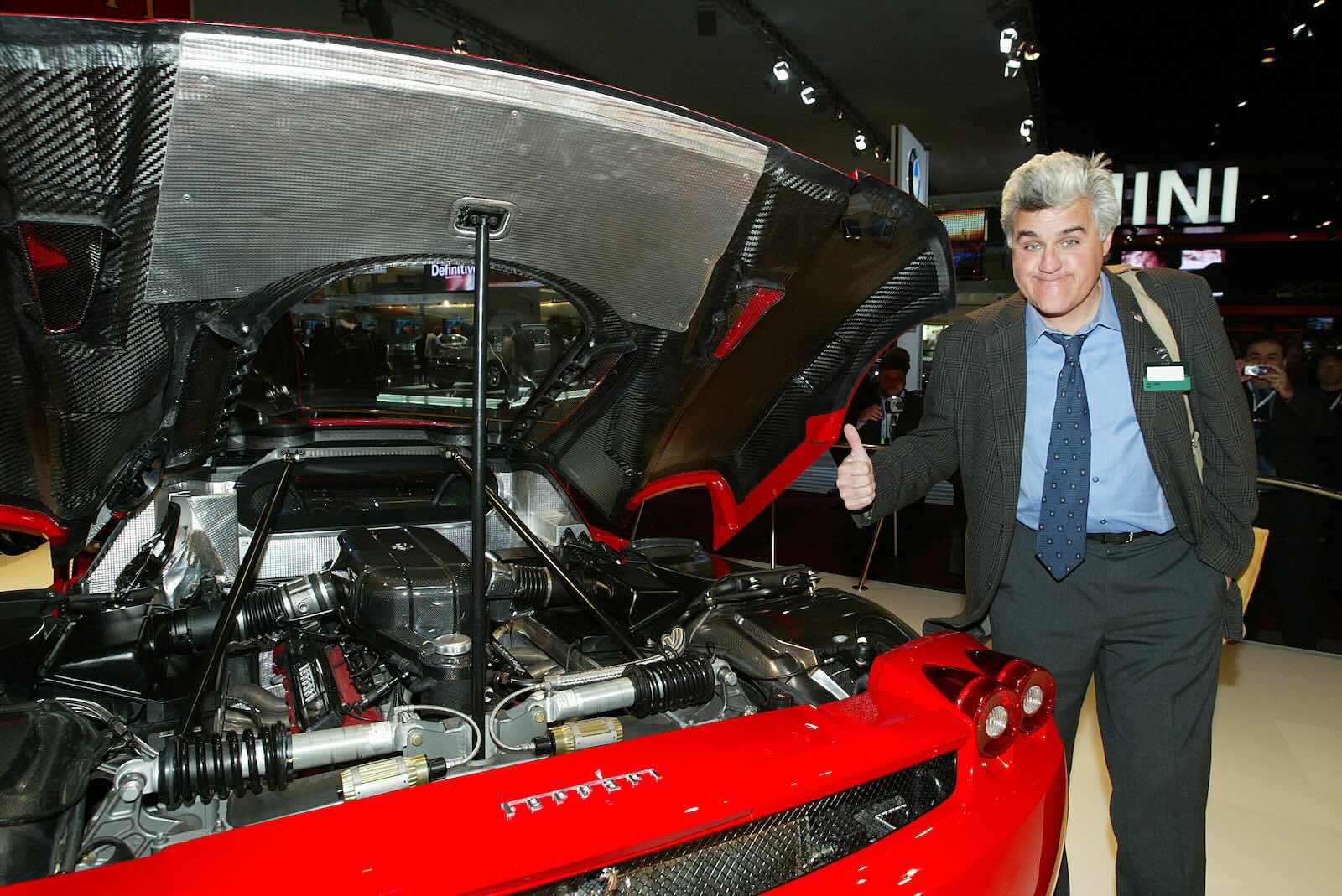 Jay Leno stands next to a Ferrari at an auto show.