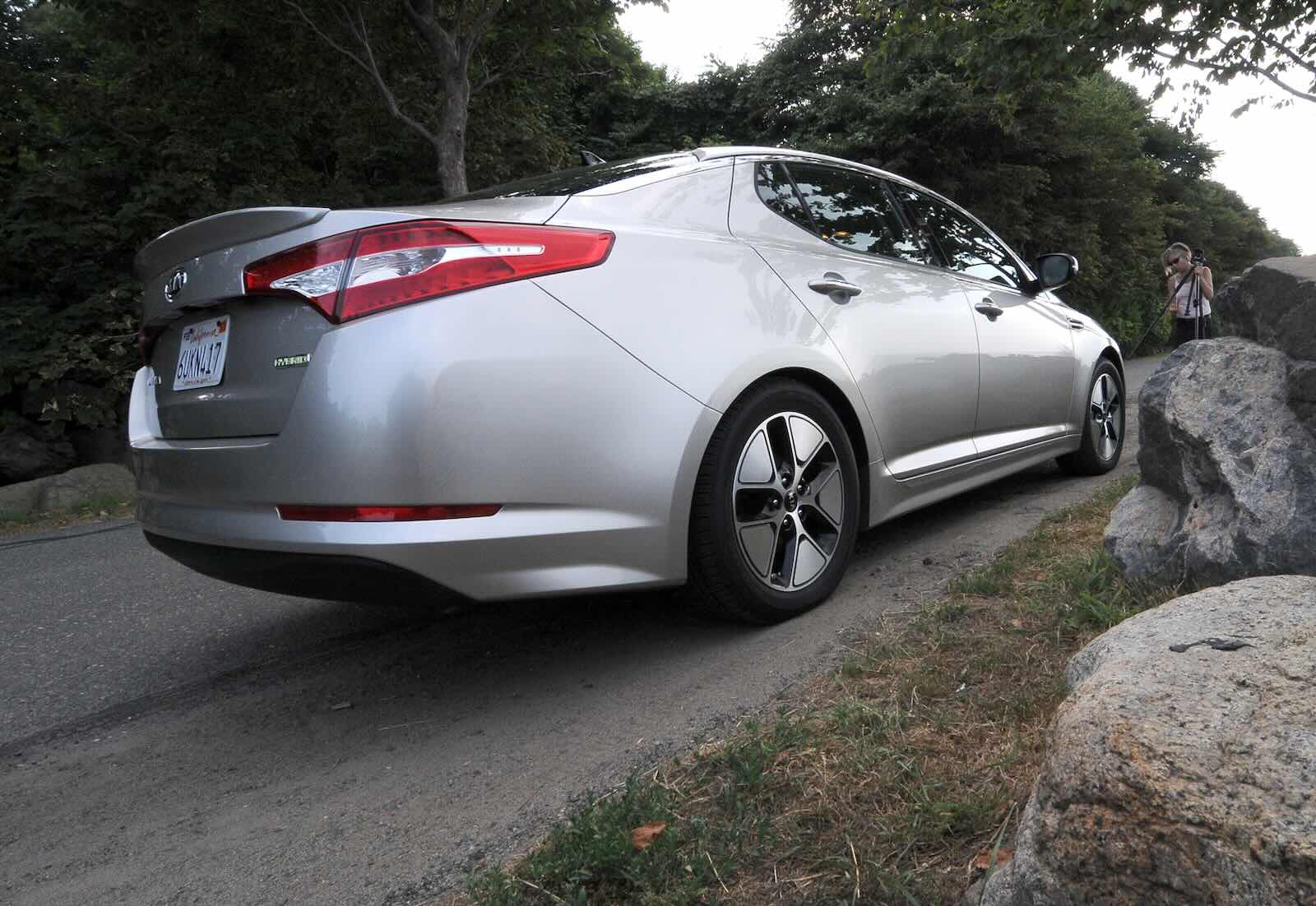 The rear of a Kia Optima sedan, with boulders visible in the foreground.