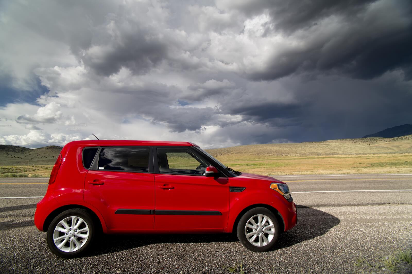 Red Kia Soul parked under dark, rolling clouds