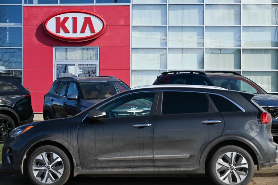 Crossovers parked under a Kia sign in front of a dealership.