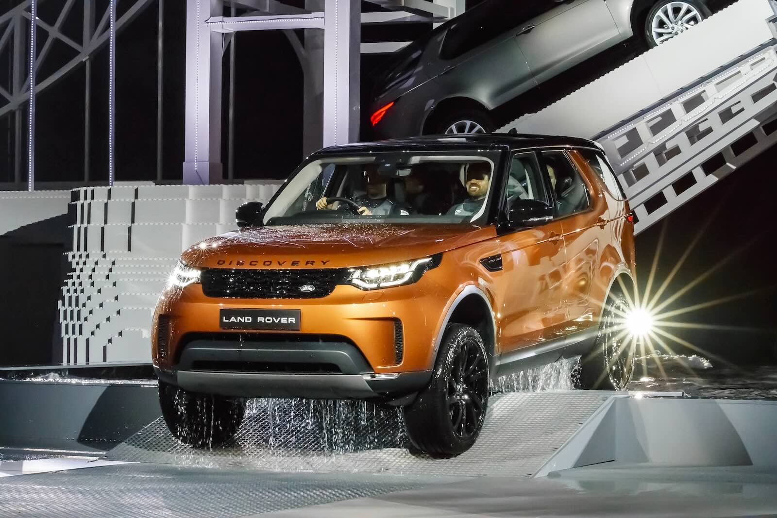 Orange Land Rover Discovery 5 Series SUV driving across a stage for its reveal ceremony