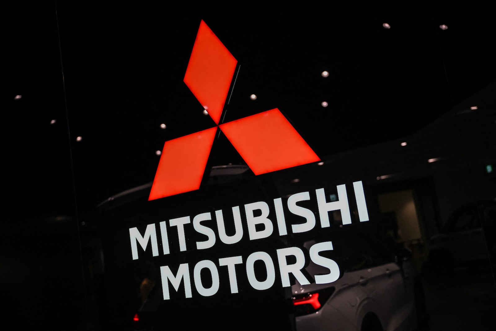The red three-point star logo of Mitsubishi Motors on a sign at an auto show.