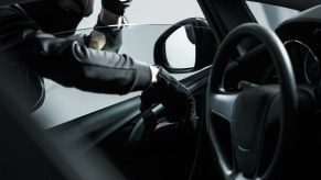 Masked burglar reaches into a car for credit cards