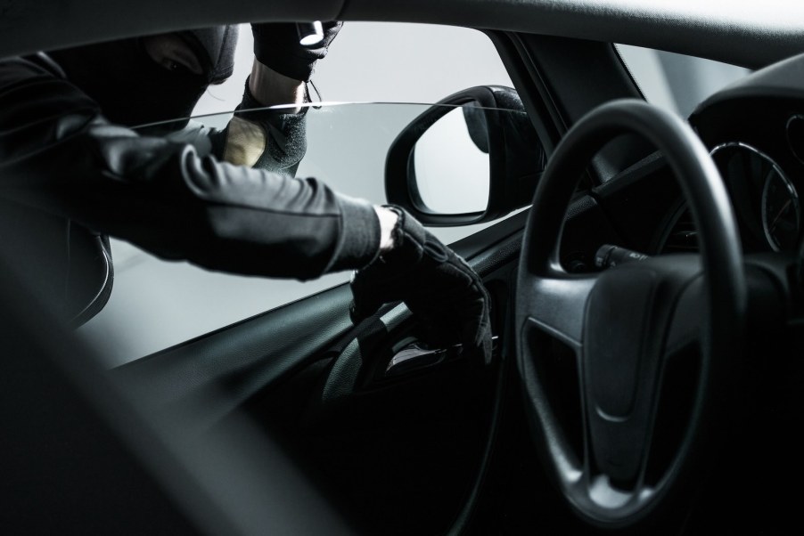 Masked burglar reaches into a car for credit cards