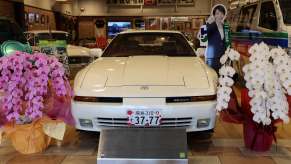White Toyota Supra in a museum, next to a cardboard standup of Toyota's Prime Minister.