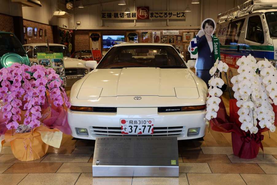 White Toyota Supra in a museum, next to a cardboard standup of Toyota's Prime Minister.