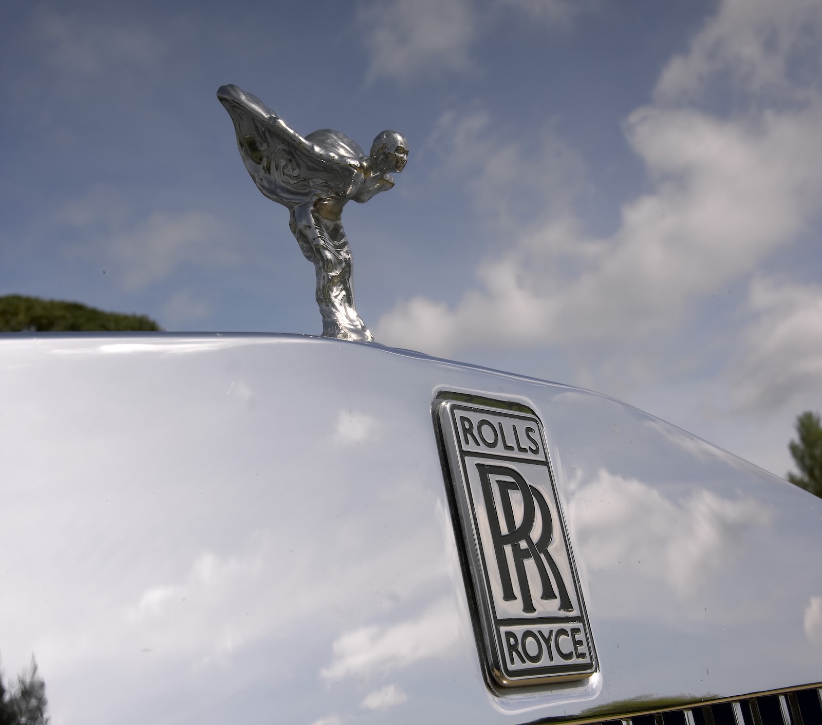 The Spirit of Ecstasy hood ornament and Rolls Royce badge on the hood of a luxury car.