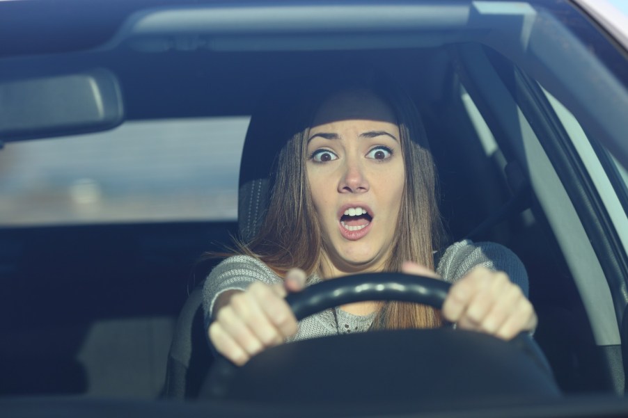 A new teen driver behind the steering wheel with a scared look on her face.