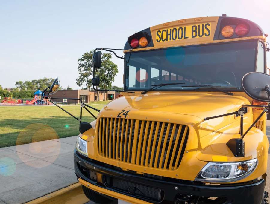 The grille of a yellow school bus, a playground visible in the background.