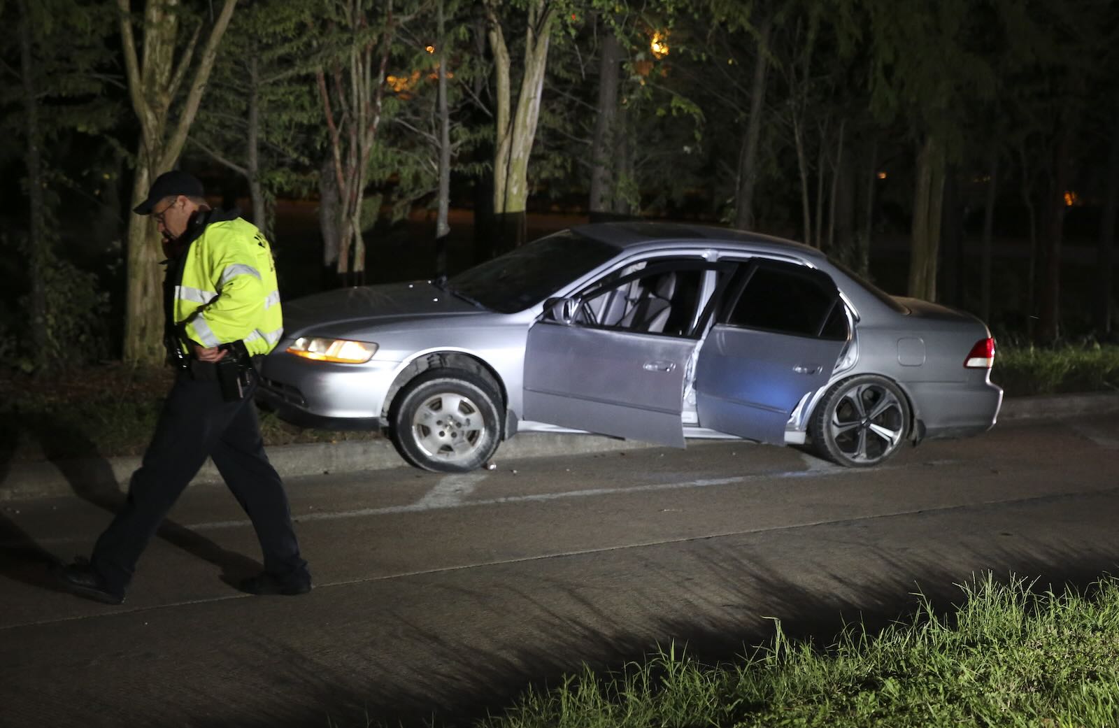 Police officer in a green jacket walks past an abandoned Honda Accord