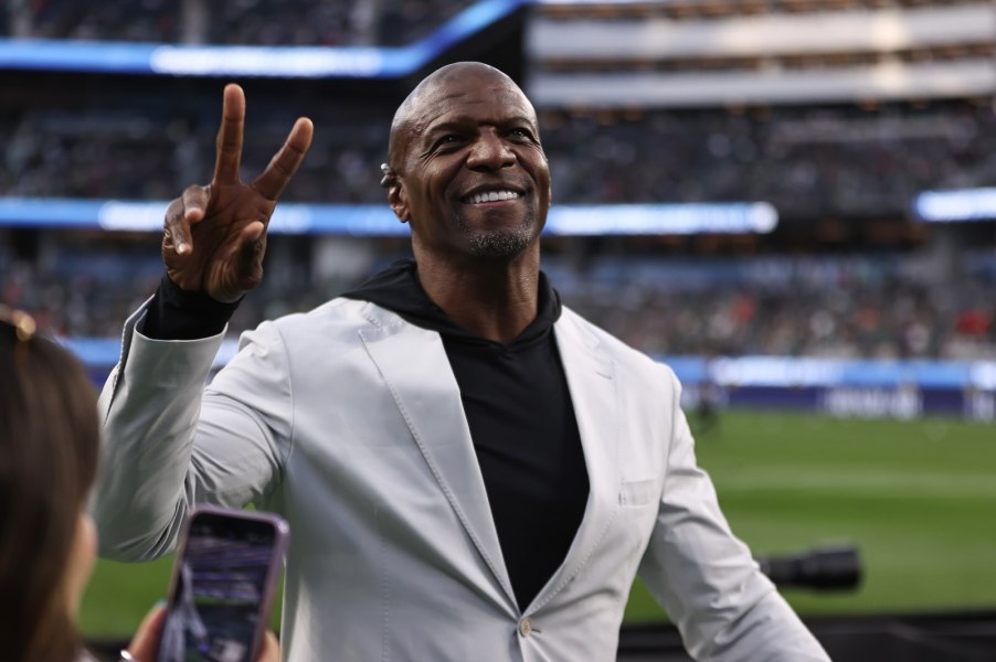 Actor Terry Crews wearing a white suit waves from a football field, the stands visible in the background.