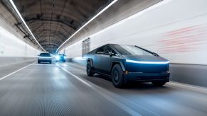 Black and silver Cybertruck driving through a tunnel at night, their headlights on.