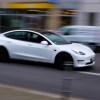 White Tesla sedan speeding down a city street, the background blurring by.