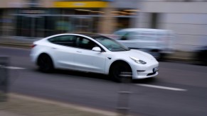 White Tesla sedan speeding down a city street, the background blurring by.