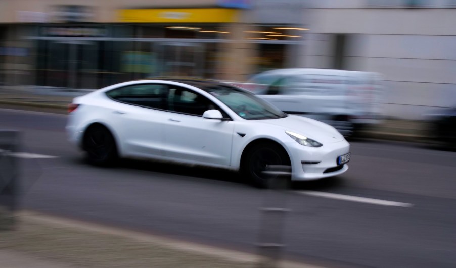 White Tesla sedan speeding down a city street, the background blurring by.