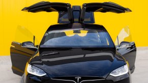 Tesla Model X with its doors open, in front of a yellow background.