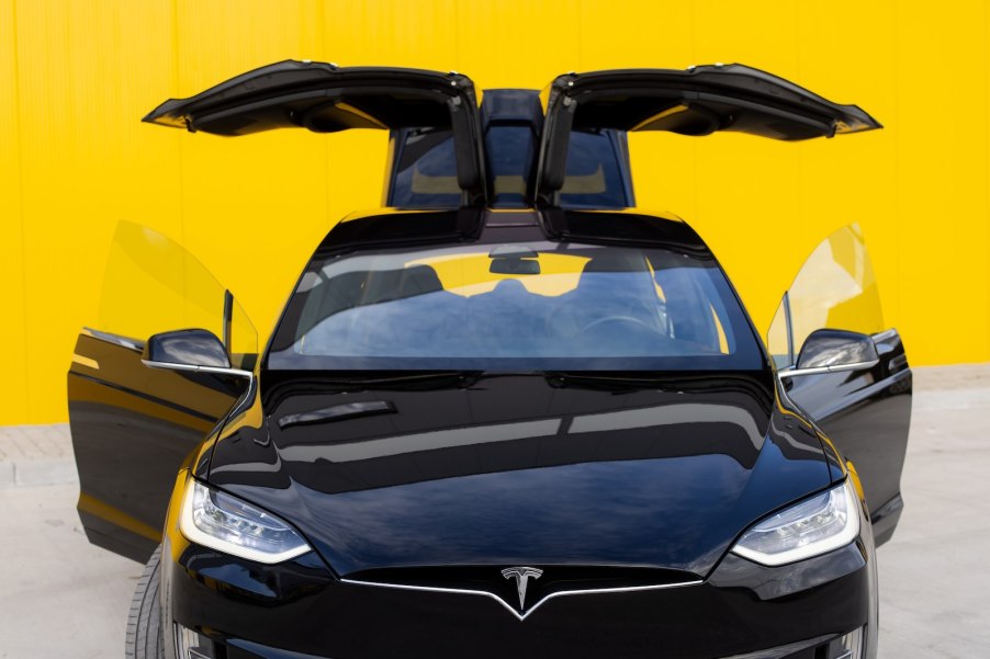 Tesla Model X with its doors open, in front of a yellow background.
