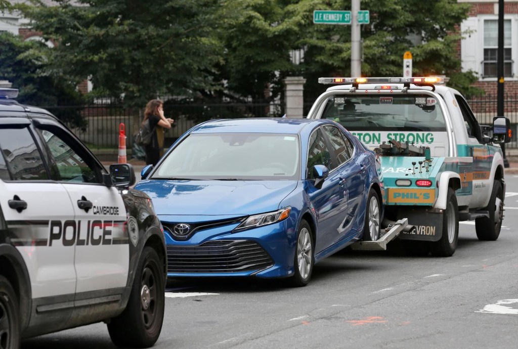 Police escort a Toyota Camry being pulled by a tow truck