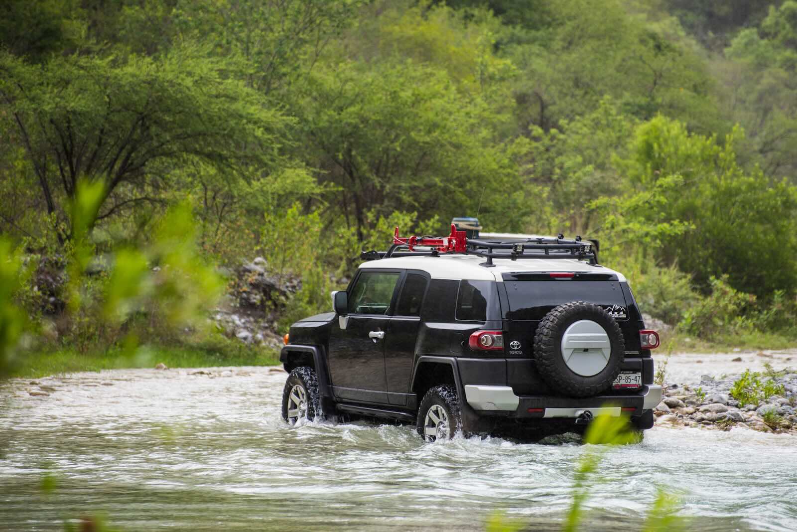 Toyota FJ Cruiser SUV fords a river, a jungle visible in the background.