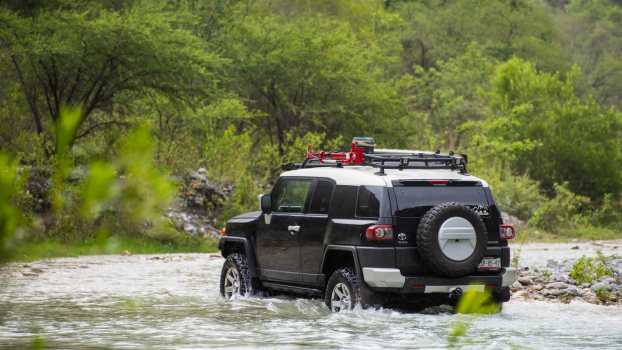 Toyota FJ Cruiser SUV fords a river, a jungle visible in the background.