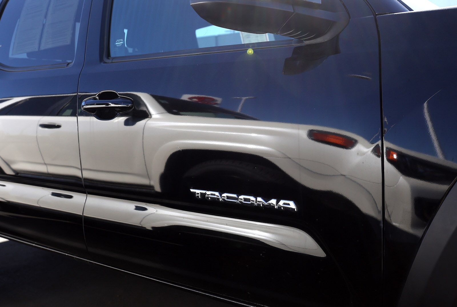 White Tacoma reflected in the paint of a black Toyota truck.