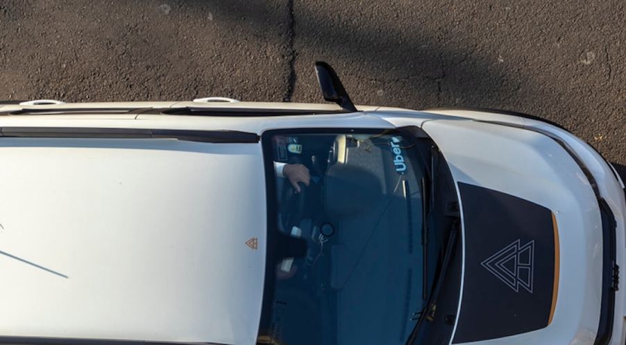 An SUV with Uber markings sits next to a curb awaiting a passenger.