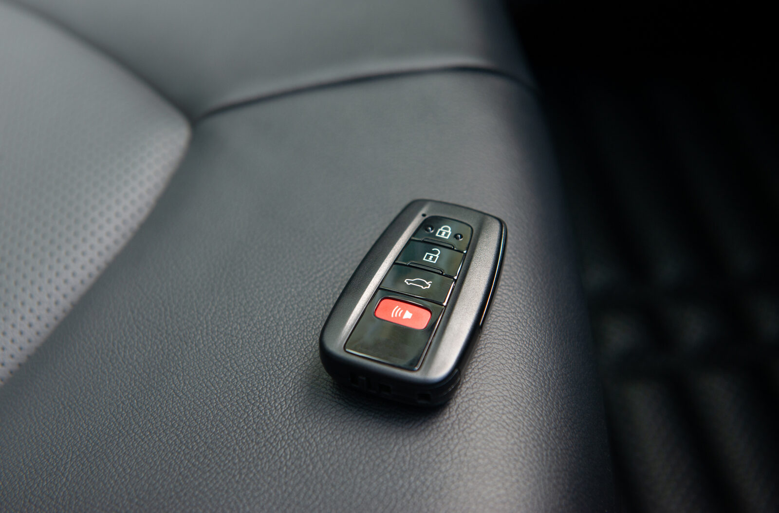 A car key fob sitting on a leather car seat in very close view