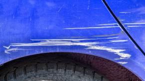 A blue car with a big paint scratch in very close view