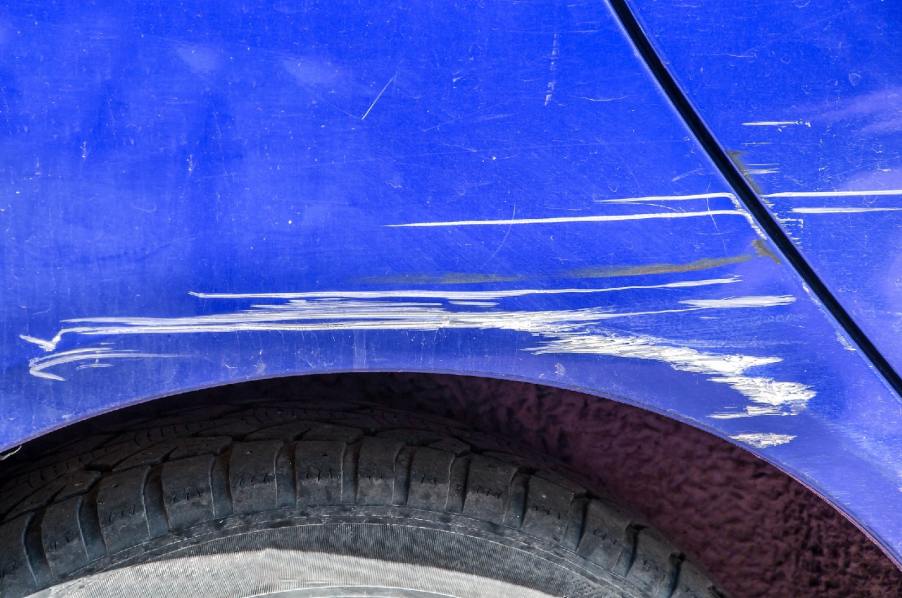 A blue car with a big paint scratch in very close view