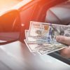 A driver holding cash in very close view of hand and side mirror
