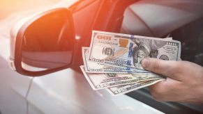 A driver holding cash in very close view of hand and side mirror