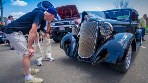 Enthusiasts examine a classic car's grille logo badge.