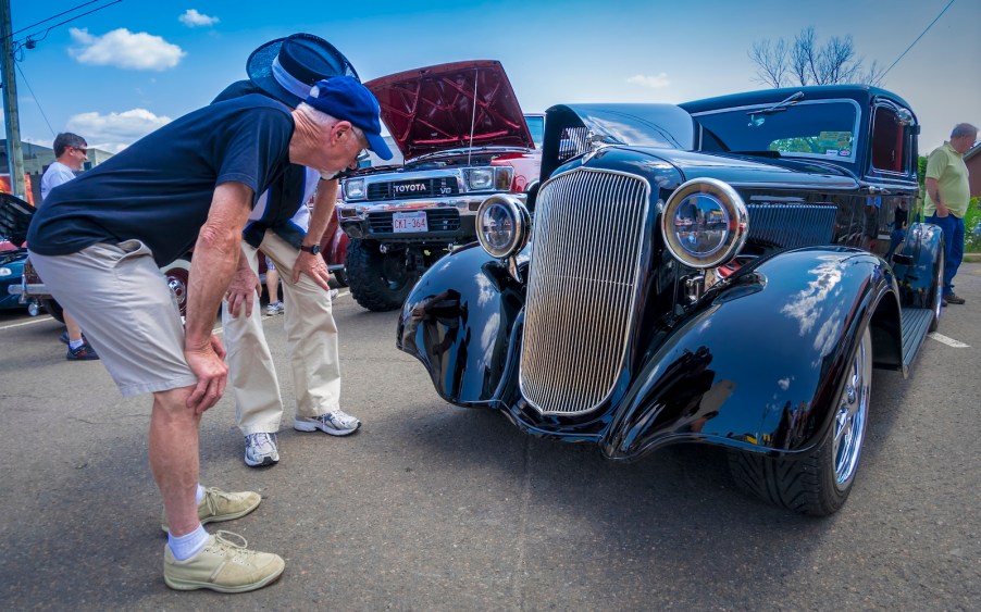 Enthusiasts examine a classic car's grille logo badge.