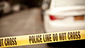 "Police line do not cross" tape strung across a road in front of blurred parked cars
