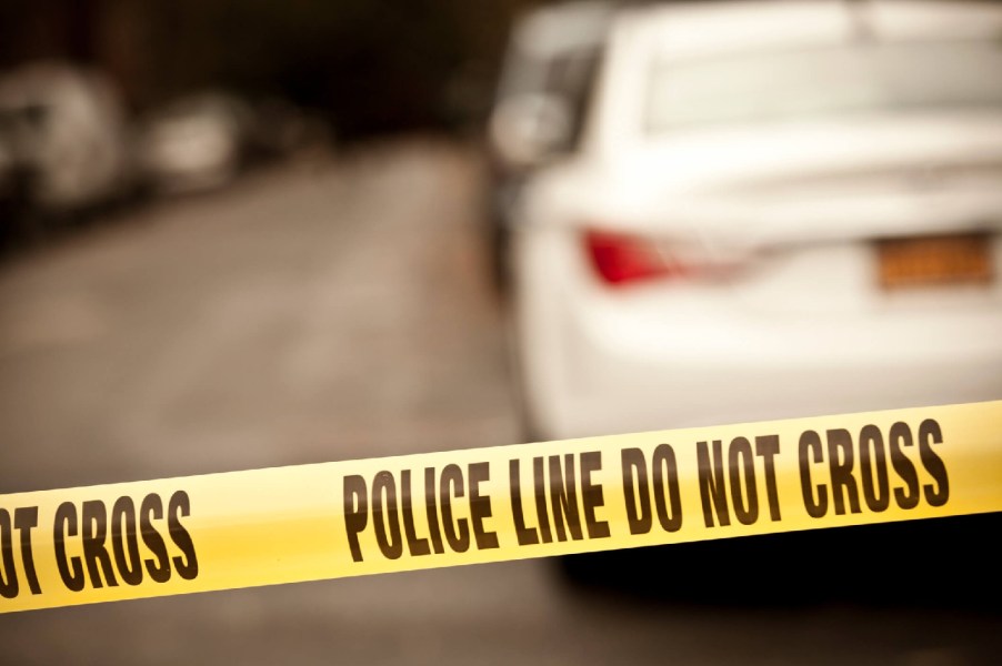 "Police line do not cross" tape strung across a road in front of blurred parked cars