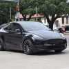 A black Tesla Model Y driving though an intersection in right front angle view