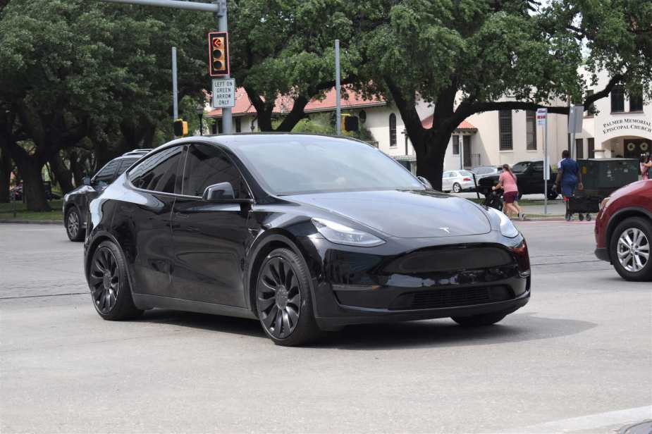 A black Tesla Model Y driving though an intersection in right front angle view