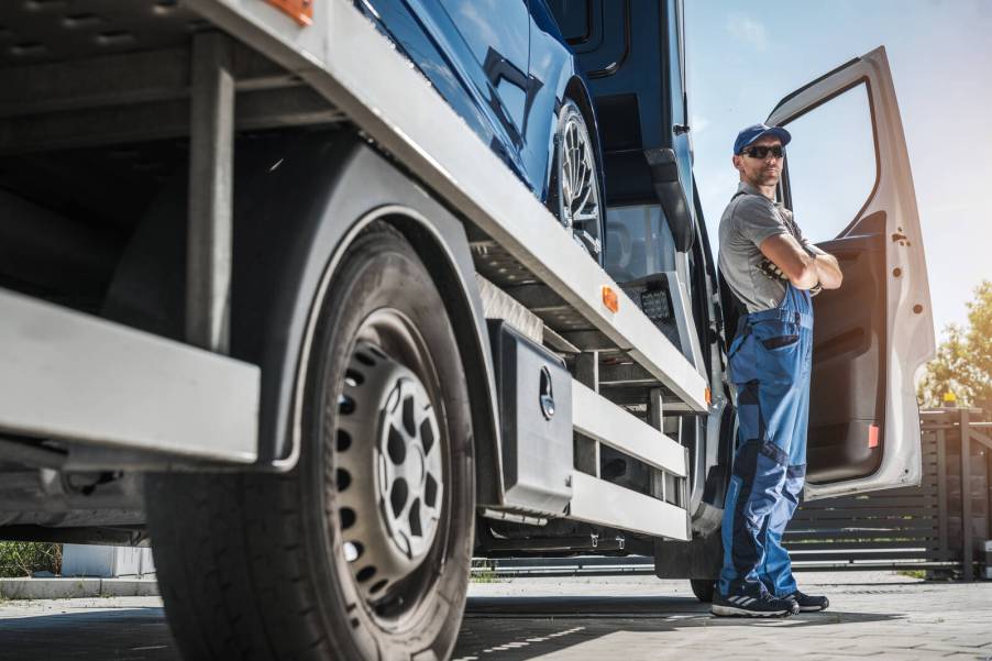 Tow truck driver stands with arms crossed in front of rig