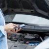 Depiction of a person using an AI tool on cell phone in front of broken down car